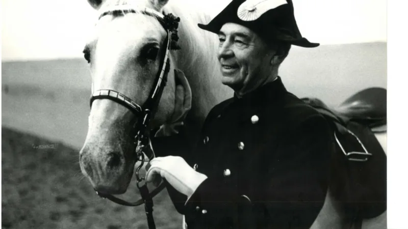 bereiter in uniform steht neben auf gold gezäumten Pferd.